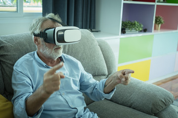 senior man happiness sitting on the sofa and playing game with VR headphone at living room for relaxing