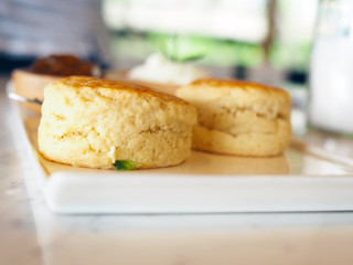 A white ceramic  tray contains butter scone served with blueberry jam and fresh butter cream. Selective focus and blurred background.