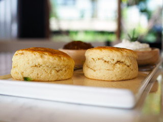 A white ceramic  tray contains butter scone served with blueberry jam and fresh butter cream. Selective focus and blurred background.