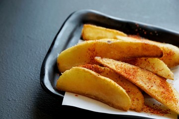 Selective focus of french fries with cayenne pepper on black plate, ready to eat or serve, on dark background
