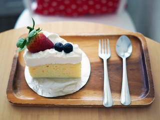 A piece of fresh cream butter cake decorated with fresh strawberry and blueberries served in wooden board. Selective focus.