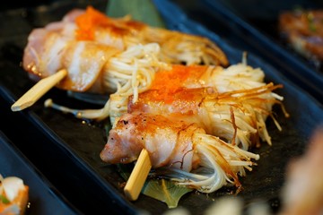 Selective focus of grilled bacon wrapped golden needle mushroom on skewer in black plate in Japanese restaurant, Enoki Bacon is japanese traditional, ready to eat or serve, on dark background