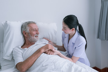 senior man with smiling nurse, takes care and discussion and cheer on bed at nursing home
