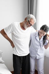 Obraz premium senior man back ache with smiling nurse, takes care and discussion on bed at nursing home