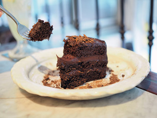 A plate of delicious homemade chocolate cake; layer chocolate sponge cake and dark chocolate, topped with cocoa flake and powder.