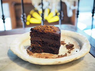 A plate of delicious homemade chocolate cake; layer chocolate sponge cake and dark chocolate, topped with cocoa flake and powder.
