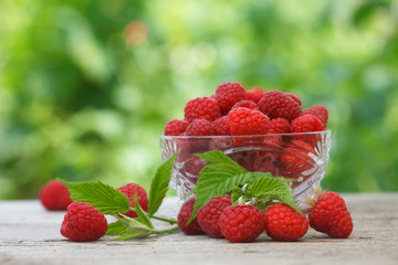 Ripe fresh organic raspberries in crystal glass bowl on wooden table, with green garden for background. Detox raspberry fruit for healthy living style.