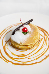 Pancakes topped with chocolate, icing sugar, and red cherry. Morning breakfast snack.