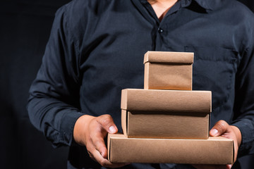 a man holding stack of different size craft boxes on black background