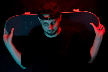 Skateboarder in black shirt with skateboard on neon light background
