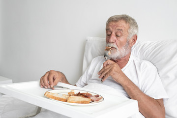 senior man with smiling nurse, takes care breakfast and discussion and cheer on bed at nursing home