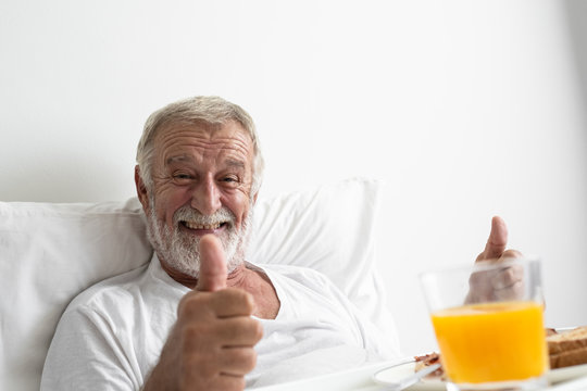senior man with smiling and thump up cheer on bed at nursing home