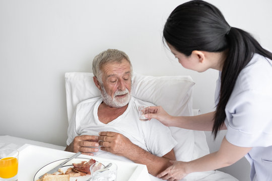 nurse give pill to senior man after breakfast and discussion on bed at nursing home