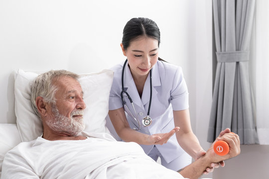 Senior Man With Smiling Nurse, Takes Care Health Check By Weight Training And Cheer On Bed At Nursing Home