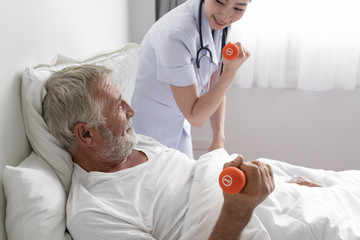 Obraz premium senior man with smiling nurse, takes care health check by weight training and cheer on bed at nursing home