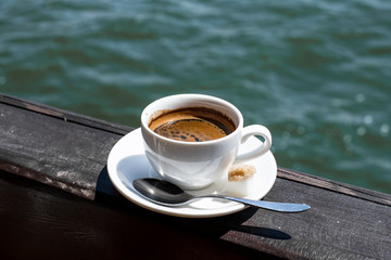 A small white porcelain espresso cup on a saucer with a teaspoon and two pieces of sugar