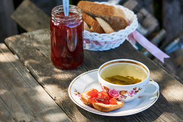Herbal tea with plum jam and bread on a wooden table