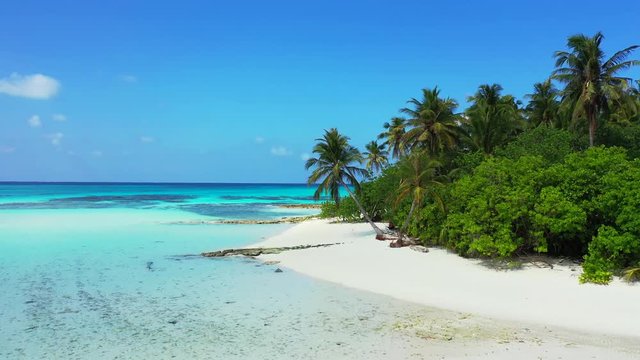Aerial perspective. Flight towards the round coast of a tropical island with palm trees on it. the shallow turquoise water of the Caribbean Sea in front of it. Dolly in