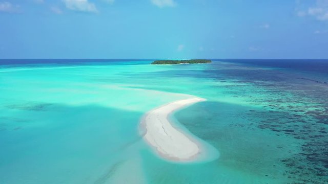 A white s-shaped sandbank surrounded by turquoise of the Caribbean Sea. Some islands in the background. Dolly in, wide angle.
