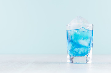 Summer cold blue lagoon drink with ice cubes in elegant shot glass on pastel mint background.