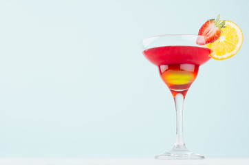 Summer fresh alcohol cocktail  with red and yellow liquor, orange slice, strawberry on soft light white and pastel green background.