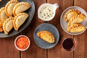 Empanadas with sauces and wine, shot from the top on a dark rustic wooden background