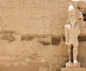 Ancient sculpture of Pharaoh on the background of a stone wall with Egyptian hieroglyphs and thematic drawings
