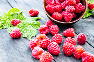 Fresh raspberry with leaves on the background of old dark boards. Selective focus.