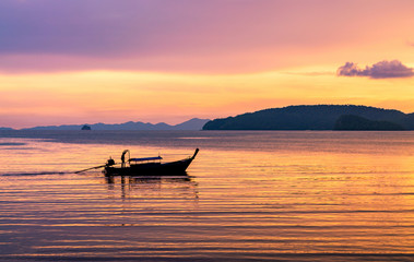 Fishing boat in the sea in the evening sunlight over beautiful big mountains background.