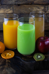 Fresh healthy orange, kiwi, apple juice, smoothie in a glass on wooden background. summer concept.