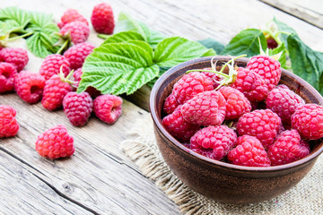 Ripe red raspberries on a bowl on the background of old boards. Selective focus.
