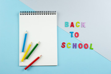 Top view of open notebook with colorful pencils and inscription by letters back to school on pastel blue and grey background. View from above, flat lay, copy space