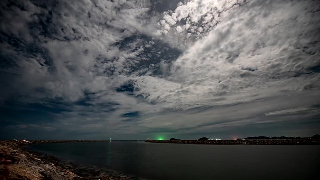 moving white clouds at blue dark night with very far green light fishing boats on curve stone beach 4k footage stock video