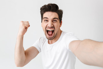 Excited happy young man posing isolated over white wall background make a selfie by camera.