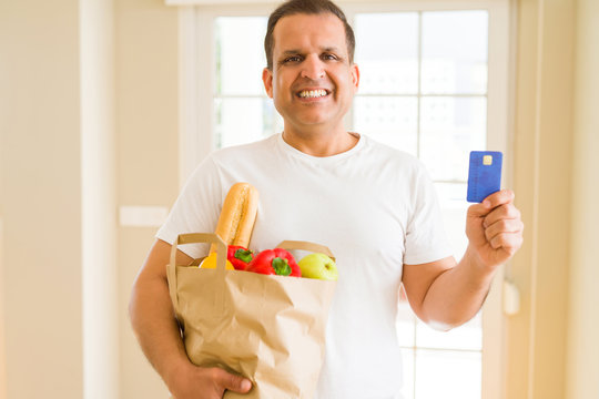Middle age man holding groceries bag and showing credit card