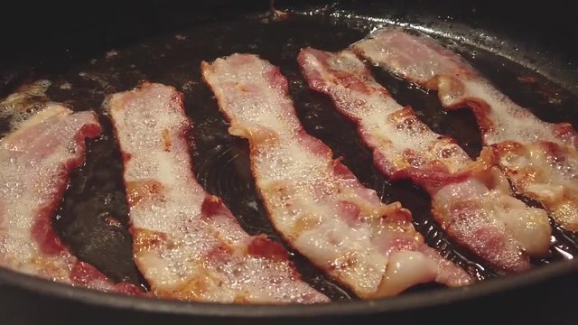 Delicious bacon sizzling in hot grease in pan
