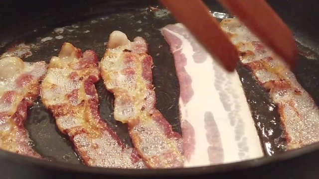 Fatty piece of bacon being put on greasy pan in slow-motion