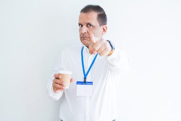 Middle age business man wearing ID card and drinking coffeeover white background pointing with finger to the camera and to you, hand sign, positive and confident gesture from the front