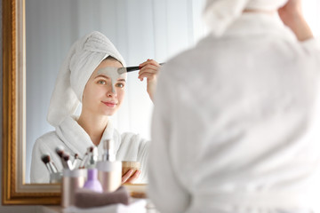 Young woman applying clay mask at home