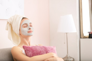Young woman with clay mask at home