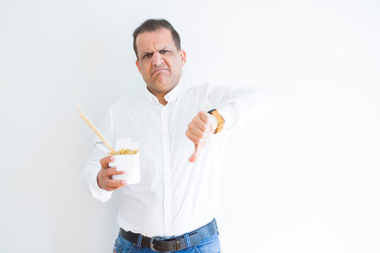 Middle Age Man Eating Asian Noodles From Take Away Carton With Angry Face, Negative Sign Showing Dislike With Thumbs Down, Rejection Concept