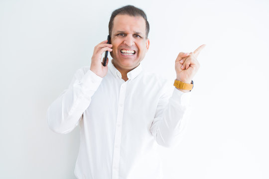 Middle age man calling using smartphone very happy pointing with hand and finger to the side