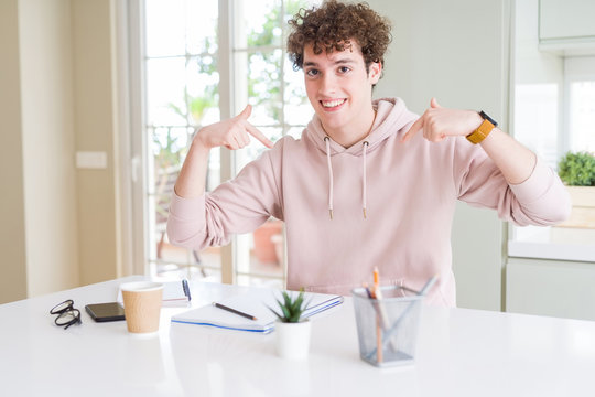 Young student man writing on notebook and studying looking confident with smile on face, pointing oneself with fingers proud and happy.