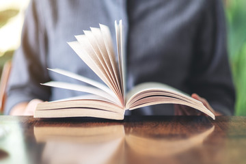 Closeup image of a woman holding and reading a vintage novel book on wooden table
