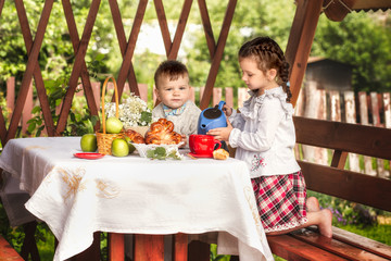  boy and girl in summerhouse drink tea with buns in summer