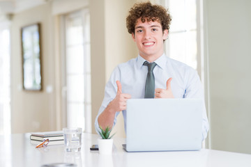 Young business man working with computer laptop at the office success sign doing positive gesture with hand, thumbs up smiling and happy. Looking at the camera with cheerful expression, winner