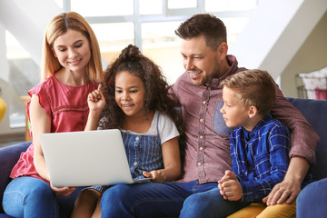Happy couple with little adopted children using laptop at home