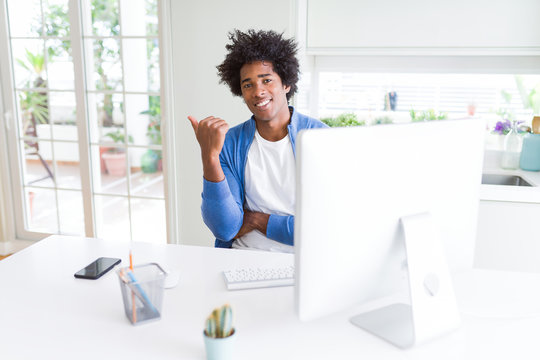 African American man working using computer smiling with happy face looking and pointing to the side with thumb up.
