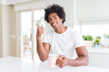 African American man with afro hair drinking a cup of coffee happy with big smile doing ok sign, thumb up with fingers, excellent sign