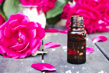 Bottle of fragrant oil with red roses on a wooden table.